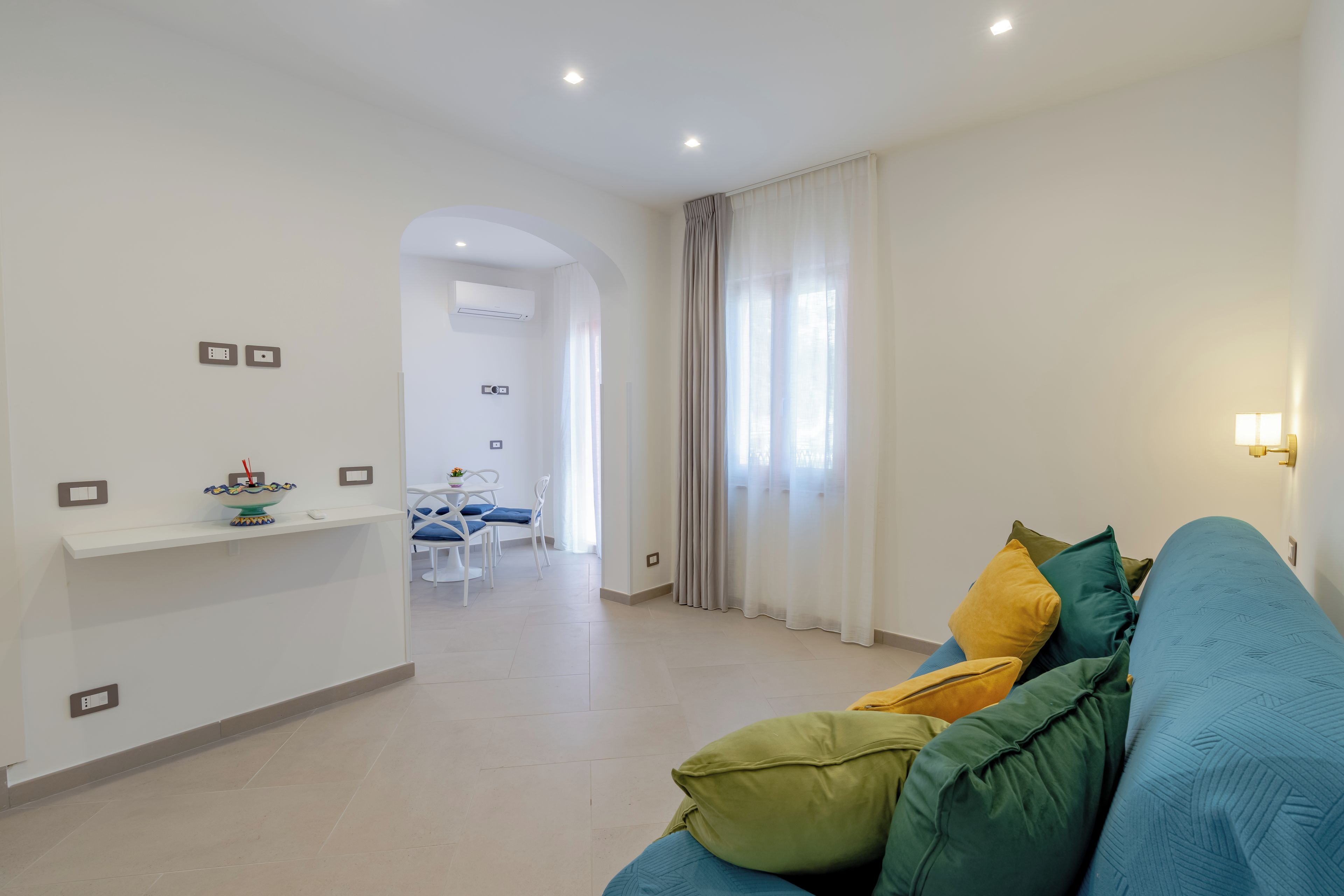 A modern living room with a sofa, a dining area with a table and chairs, and a kitchen area with a countertop and appliances.