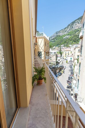 A balcony with a potted plant, a view of a street with parked cars, and buildings in the background.