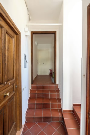 A hallway with a wooden door, a tiled staircase, and a white wall. - Residence Palazzo Verderame (Amalfi)