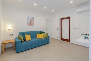 A living room with a blue sofa, a wooden table, and a painting on the wall. - Residence Palazzo Verderame (Amalfi)