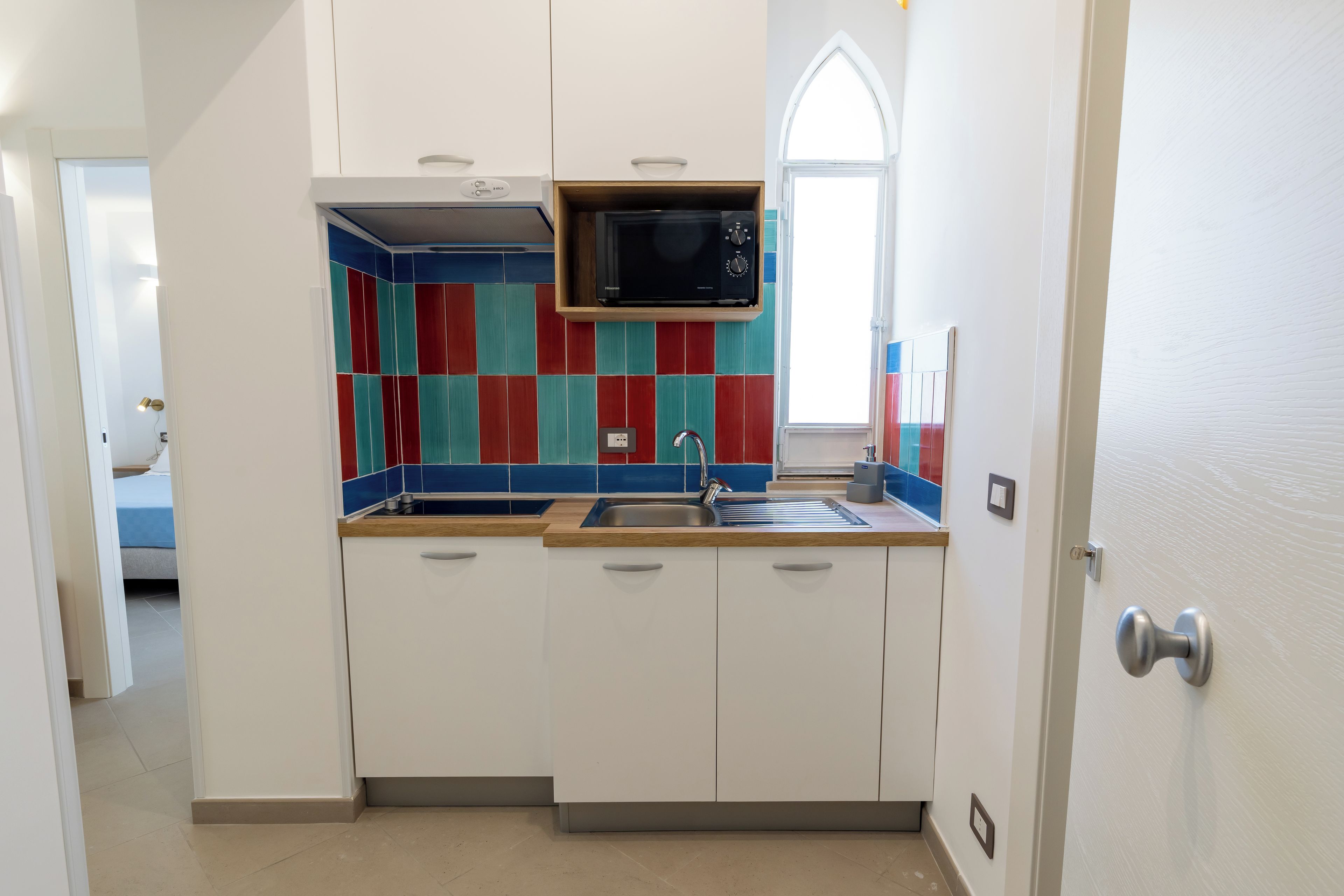 A compact kitchen with white cabinets, a microwave, and a colorful backsplash.