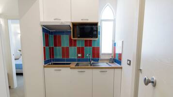 A compact kitchen with white cabinets, a microwave, and a colorful backsplash.