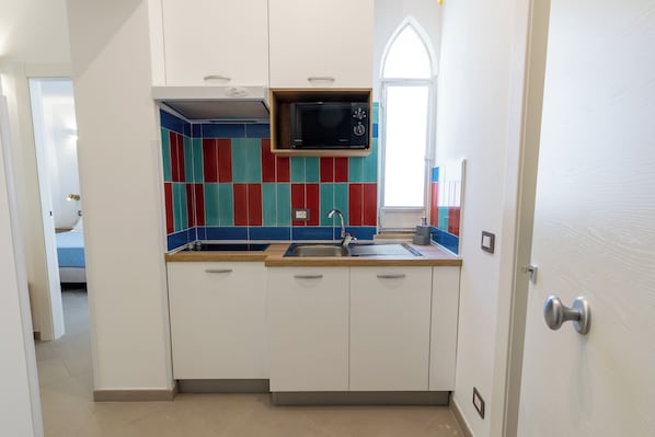 Cocina compacta con armarios blancos, un microondas y un protector contra salpicaduras colorido.