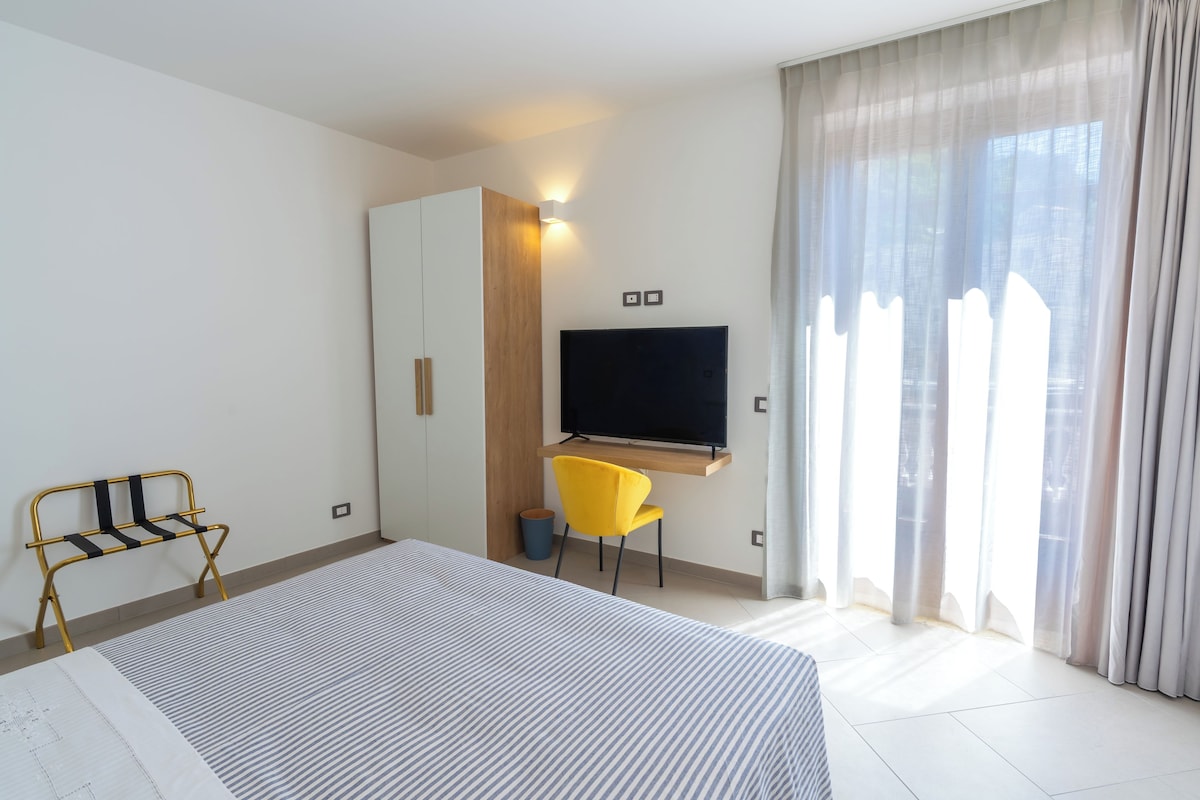 A hotel room with a bed, a desk with a chair, a television, and a wardrobe.