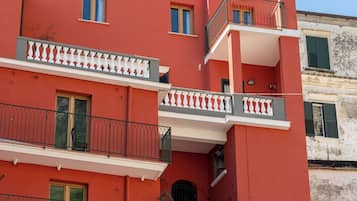 A multi-story building with balconies and windows, featuring a red facade and green shutters.