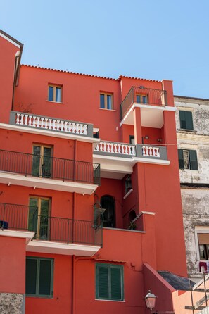 A multi-story building with balconies and windows, featuring a red facade and green shutters. - Residence Palazzo Verderame (Amalfi)