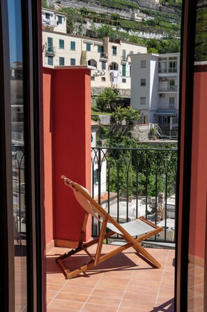 A balcony with a wooden chair and a red wall.