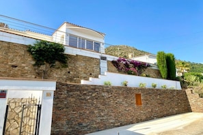 A modern house with a stone facade, a white upper level, and a small garden with purple flowers. - Holiday home in Roses with swimming pool (Roses)
