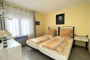 A bedroom with two beds, a bedside table, a lamp, and a window with curtains. - Holiday home in Roses with swimming pool (Roses)