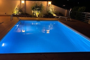 A swimming pool at night with a metal ladder, a lounge chair, and potted plants. - Holiday home in Roses with swimming pool (Roses)