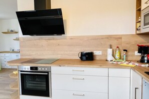 A kitchen with a built-in oven, a microwave, a coffee maker, and a flat-screen TV mounted on the wall. - Duhner Allee 10, "Litfaß 12" (Cuxhaven)