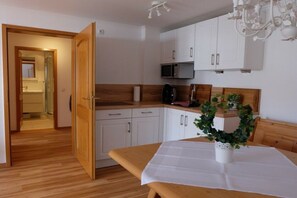 A kitchen with white cabinets, a wooden countertop, a microwave, and a dining table with a white tablecloth. - Allgäu Hearts 1 and 2 (Kornau\/Oberstdorf)