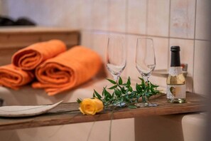 Ein Holztisch mit gerollten orangefarbenen Handtüchern, zwei leere Gläser, eine Champagnerflasche, ein weißer Teller und eine gelbe Rose.