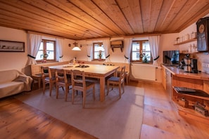 A cozy room with a wooden dining table, chairs, a sofa, and a kitchen area with shelves and appliances. - Holiday home in Mauth with barbecue (Mauth)
