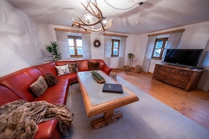 Ein Wohnzimmer mit einem roten Ledersofa, einem Holztisch, einem Fernseher und einem Kamin.