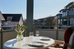 A table set with plates, cutlery, and a vase of flowers on a balcony with a view of buildings. - Holiday apartment with 1 bedroom (Langenargen)