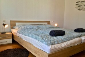 A single bed with a patterned bedspread, two pillows, a bedside lamp, and a small rug on a wooden floor. - Holiday apartment with 1 bedroom (Langenargen)