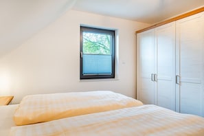 Ein Schlafzimmer mit zwei Betten, einem Fenster mit Jalousien und einem Kleiderschrank.