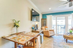 A modern living room with a dining area, a television mounted on the wall, and a view of the outside through large windows. - Galveston Condo (Galveston)