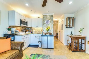 A modern kitchen with white cabinets, a central island, and a microwave. - Galveston Condo (Galveston)