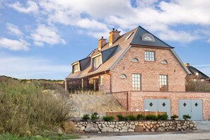 A two-story brick house with a sloped roof, a stone retaining wall, and a garage with two doors. - Holiday home in Hörnum with swimming pool (Hörnum)