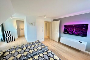 Ein modernes Schlafzimmer mit einem Bett, einem an der Wand befestigten Fernseher und einer Tür zu einem anderen Raum.