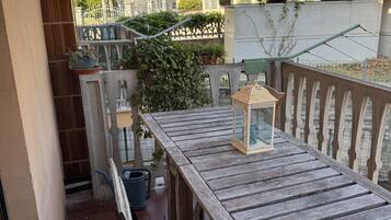 Ein Holztisch mit einer Laterne auf einem Balkon mit Blick auf einen Garten und Nachbarhäuser.