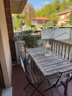 A wooden table with a lantern on a balcony with a view of a garden and neighboring houses. - The House of the "Sciure" (Ferrere)