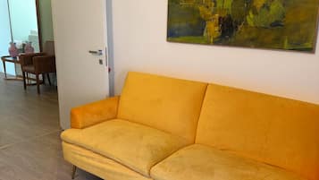 Ein Zimmer mit einem gelben Sofa, einem Gemälde an der Wand und einer Tür zu einem anderen Raum.