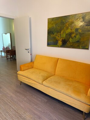 Une pièce avec un canapé jaune, un tableau accroché au mur et une porte qui donne sur une autre pièce.
