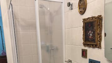 Eine Dusche mit Glastür, ein Holzschrank und eine mit Bildern gestaltete geflieste Wand.
