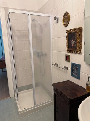 Une douche avec une porte en verre, un meuble en bois et un mur carrelé orné d’œuvres d’art encadrées.