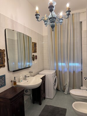 A bathroom with a large mirror, a sink, a washing machine, a toilet, and a chandelier.
