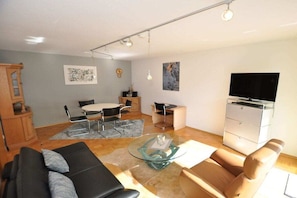 A modern living room with a sofa, armchair, glass coffee table, and a flat-screen TV. - Holiday apartment with 1 bedroom (Schwangau)