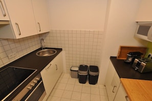 A compact kitchen with a sink, stove, and trash bins. - Holiday apartment with 1 bedroom (Schwangau)