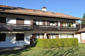 A two-story building with a balcony, a well-maintained lawn, and a clear sky. - Holiday apartment with 1 bedroom (Schwangau)