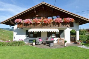 A chalet with a balcony adorned with flowers, a covered patio with seating, and a view of the surrounding landscape. - Wildbach - Herb Family (Rettenberg)
