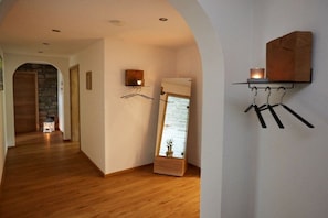 A hallway with wooden flooring, a stone wall, a hanging coat rack, and a small table with a candle. - Wildbach - Herb Family (Rettenberg)