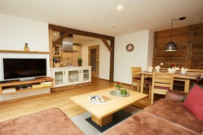 A living room with a flat-screen TV, a wooden coffee table, a sofa, and a dining area with a wooden table and chairs. - Wildbach - Herb Family (Rettenberg)