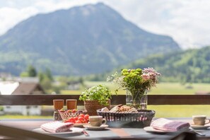 Ein gedeckter Tisch mit einem Brotkorb, einem Blumenstrauß und einer Kaffeetasse, im Hintergrund eine Berglandschaft.