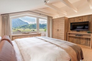 Ein Schlafzimmer mit einem großen Bett, einem an einem Holzkasten montierten Fernseher und einem Fenster mit Blick auf Berge.