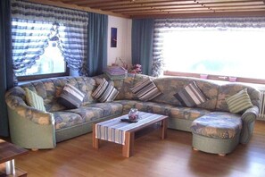 A living room with a sectional sofa, a wooden coffee table, and a window with curtains. - All Inclusive Card Holiday Apartment 1-Heigl (Viechtach)