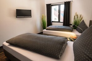 A hotel room with two beds, a flat-screen TV mounted on the wall, a window with curtains, and a small table with a remote control and a book. - Holiday apartment with 2 bedrooms (Oberstdorf)