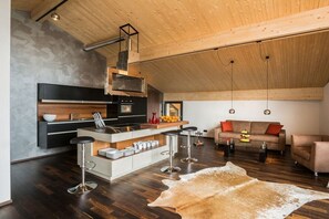 A modern kitchen with a central island, bar stools, and a dining area with a sofa and coffee table. - Holiday apartment with 2 bedrooms (Oberstdorf)