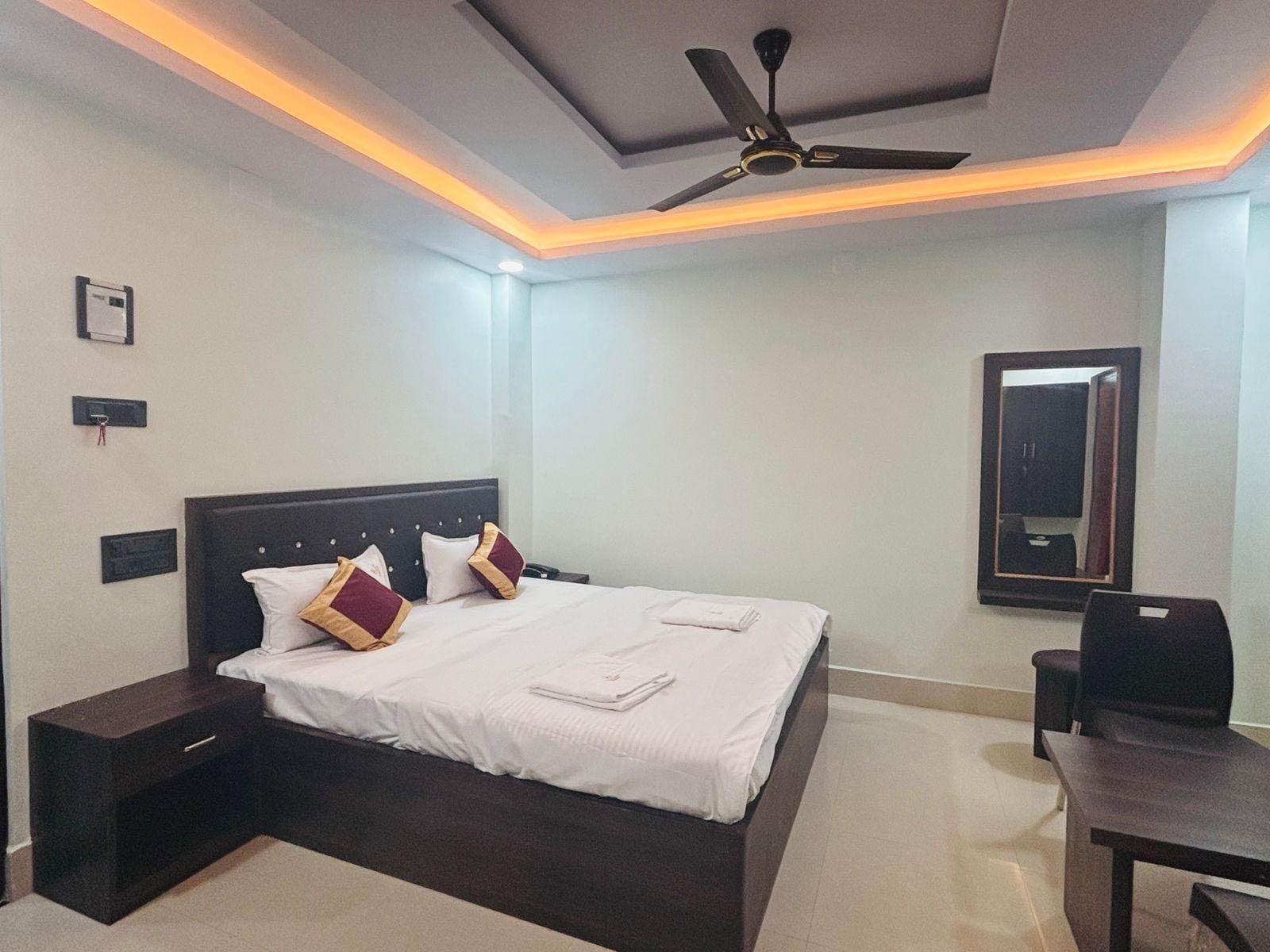 Une chambre d’hôtel équipée d’un lit, d’un bureau, d’une chaise, d’un ventilateur de plafond et d’un miroir.