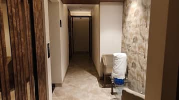 Ein schmaler Flur mit einem Stuhl, einem Tisch, einer Tür mit vertikalen Jalousien und einer Wand mit Muster.
