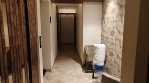 A narrow hallway with a chair and a table, a door with vertical blinds, and a patterned wall.