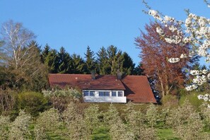 A house with a red roof, surrounded by trees and blooming flowers. - Holiday apartment with 2 bedrooms (Wasserburg)