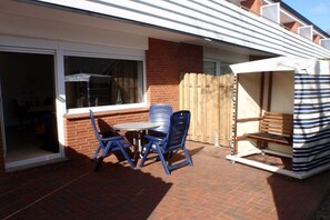 A patio with a table and chairs, a wooden fence, and a striped awning. - Mövennest, holiday apartment 2 in the Süderhaus (Borkum)