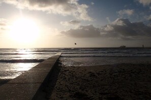 A beach with a concrete walkway leading to the water, waves, and a ship in the distance. - Mövennest, holiday apartment 2 in the Süderhaus (Borkum)